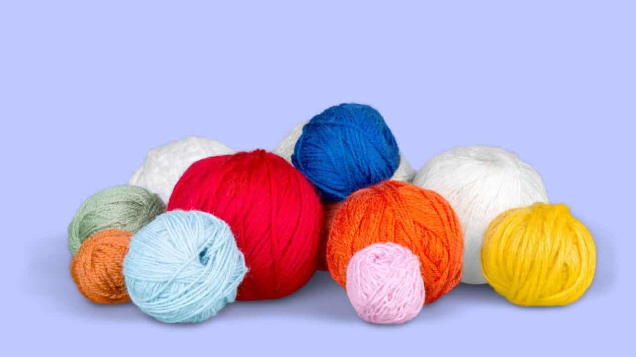 several balls of yard in multiple colors on light purple background