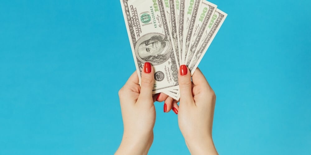 woman's hands holding $100 dollar bills