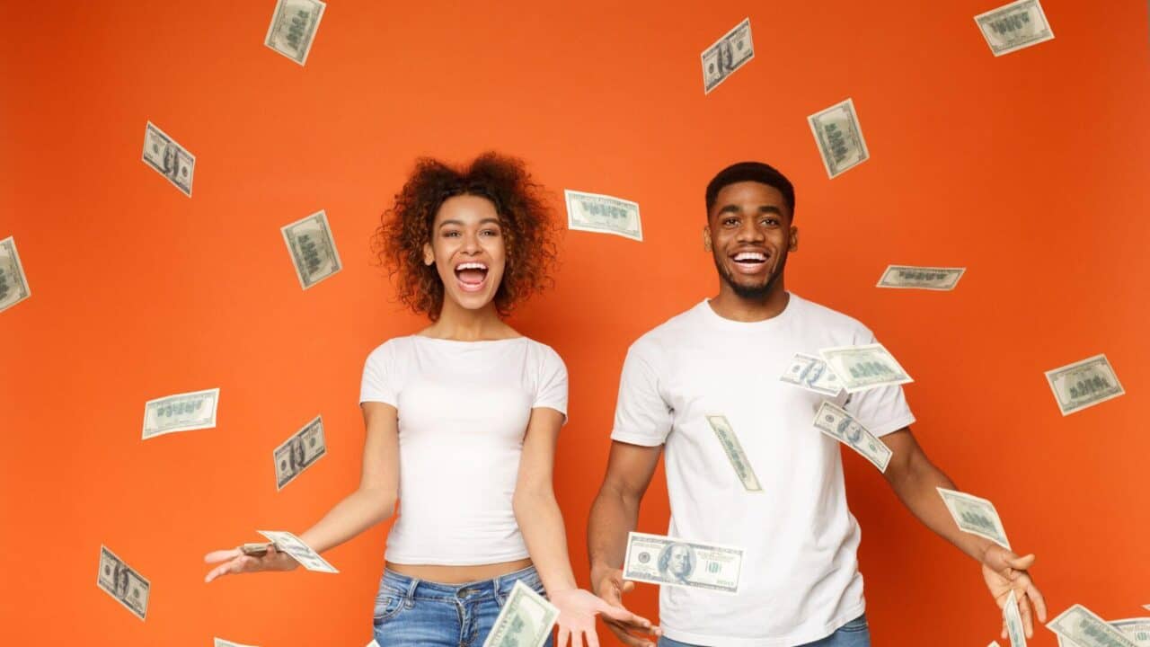 African American couple happy because money is falling on them orange background