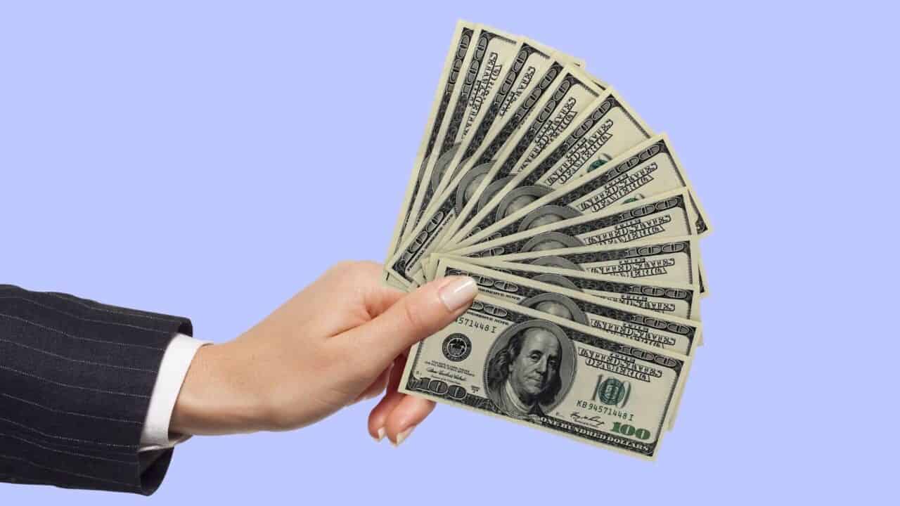 business woman's hand holding money in fan with purple background