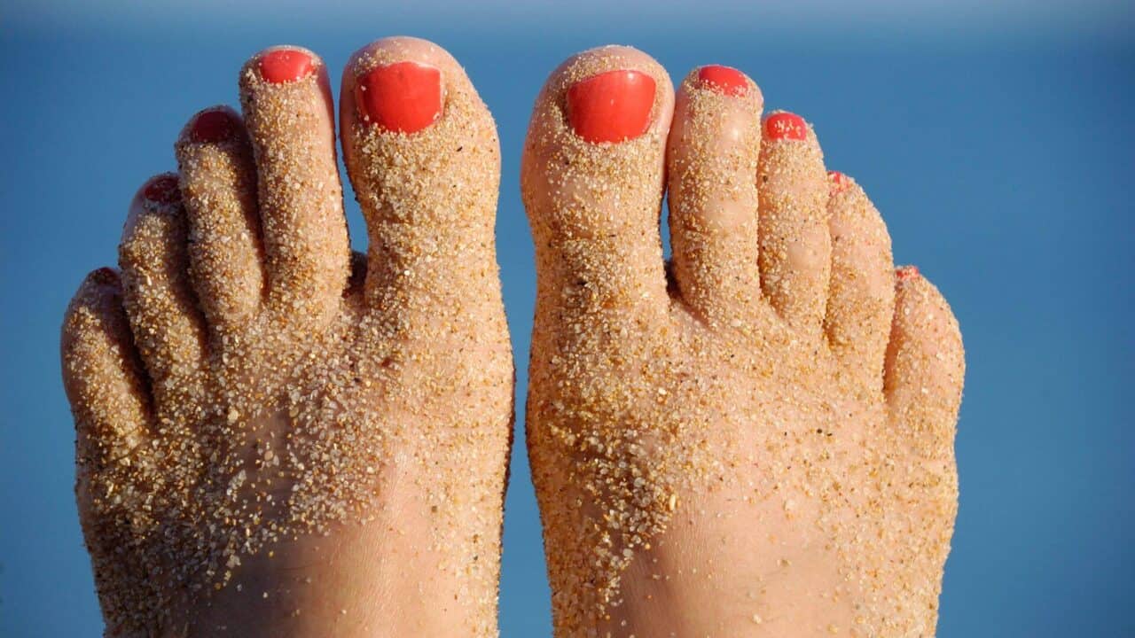 graphic of close up photo of woman's feet toes painted red with beach sand on feet blue background